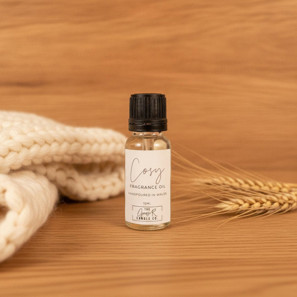 Cosy Fragrance Oil by The Gower Candle Co. on rustic oak wood with a cream knit blanket and dried wheat