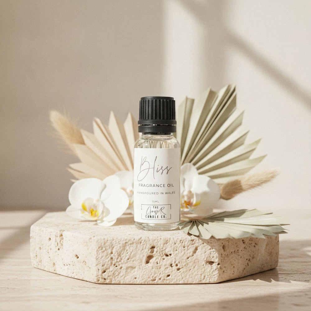 Bliss Fragrance Oil by The Gower Candle Co. on a travertine pedestal with white orchids and dried palm leaves