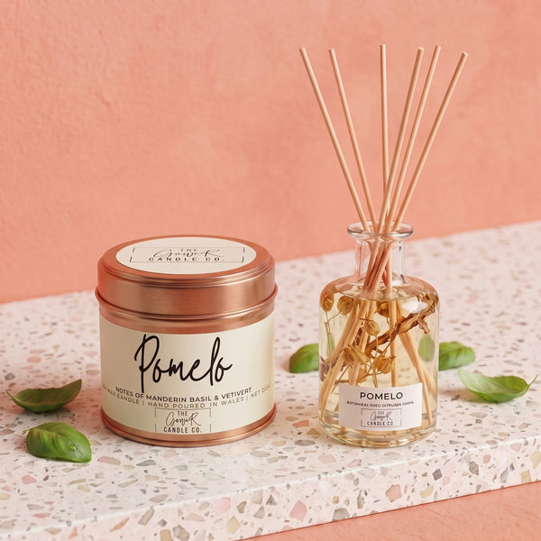 Pomelo botanical reed diffuser and matching rose gold candle bundle styled on terrazzo with basil leaves